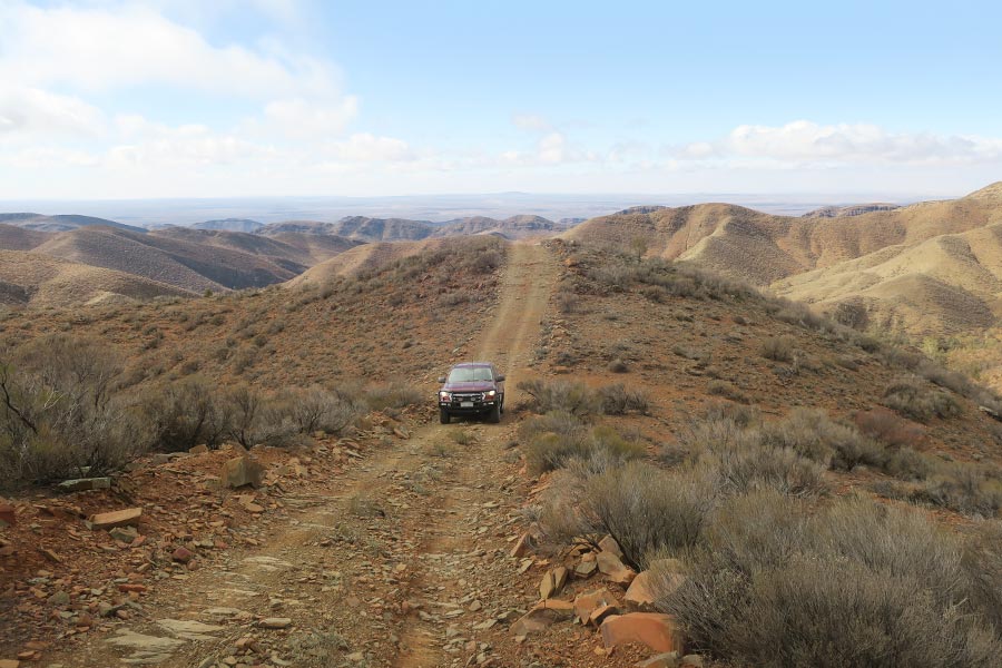 A car drives along a track with a view of ranges in the distance