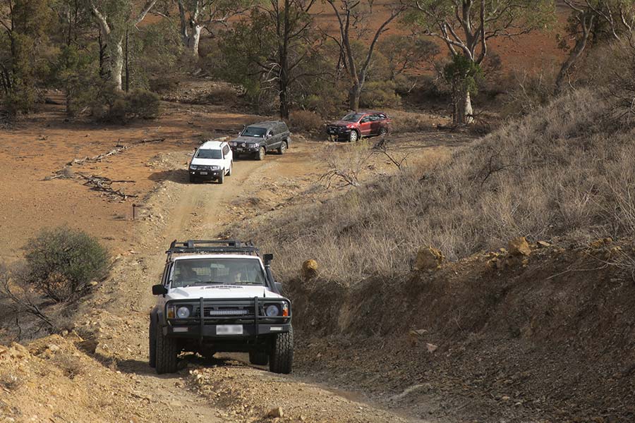 Three vehicles at the base of a hill behind an old Nissan patrol climbing the hill