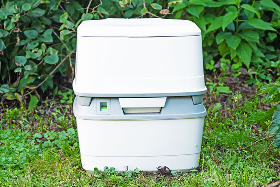 From chemical cassettes to composting solutions, the topic of portable toilets can get a little deep for the first-timer A portable toilet sitting on a green lawn in front of a green hedge.