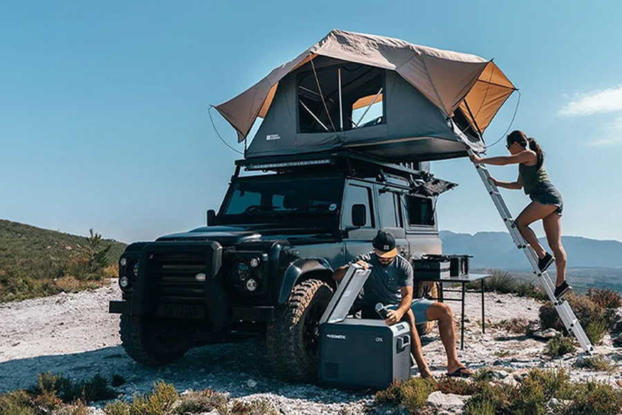 Tune in as our gear gurus unpack what's worth watching in the world of outdoor gear! Two campers on a beach, one climbing the ladder up to the roof top tent on their 4WD, the other reaching into an esky.