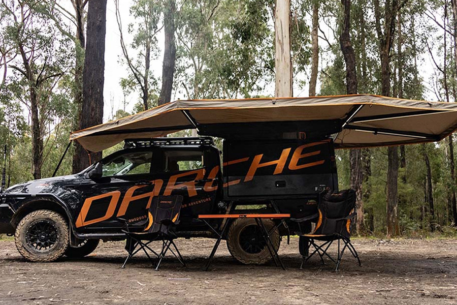 Tune in for some straight-up talk about keeping your awning upright! A Darche branded vehicle with a freestanding awning, two camp chairs, and a table.
