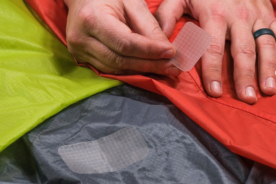 Ben and Lauren are back with a practical episode all about fixing your camping shelter A close-up of a hand applying a repair patch to a green and orange tent.