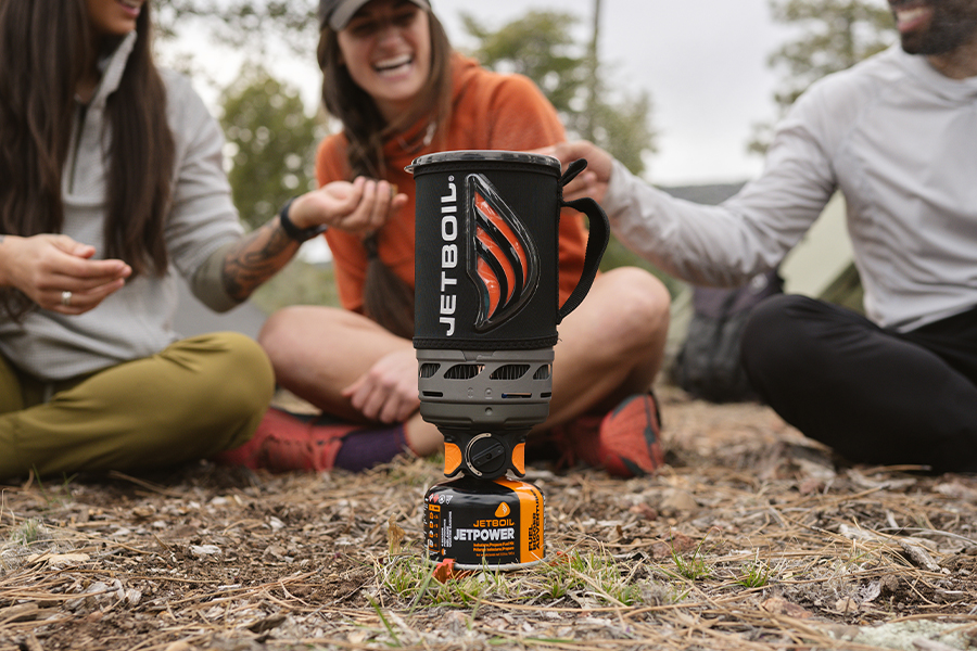 A group of three campers sit around a JetBoil hiking stove. 
