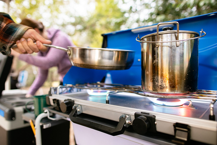 A hand placing a pan on a blue camp stove. 