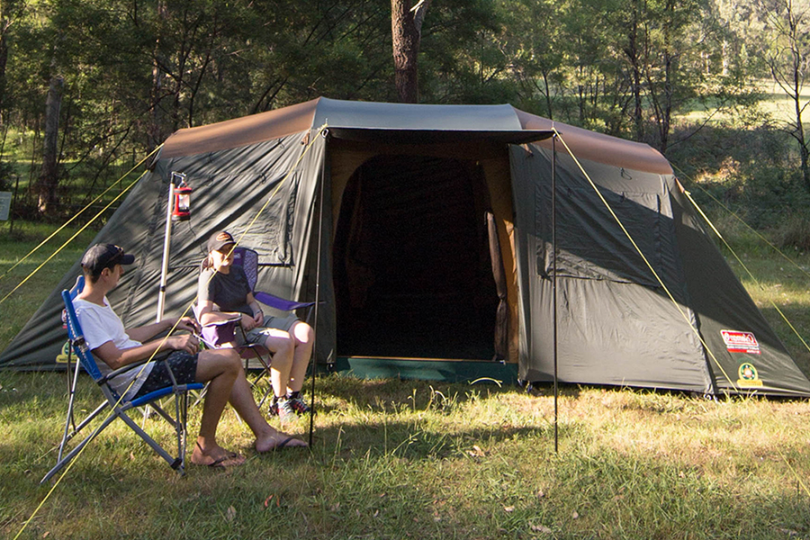 Tune in for a comprehensive guide that proves the 'better' tent is simply what suits your style of adventure Two campers sitting outside a Coleman tent in the bush.