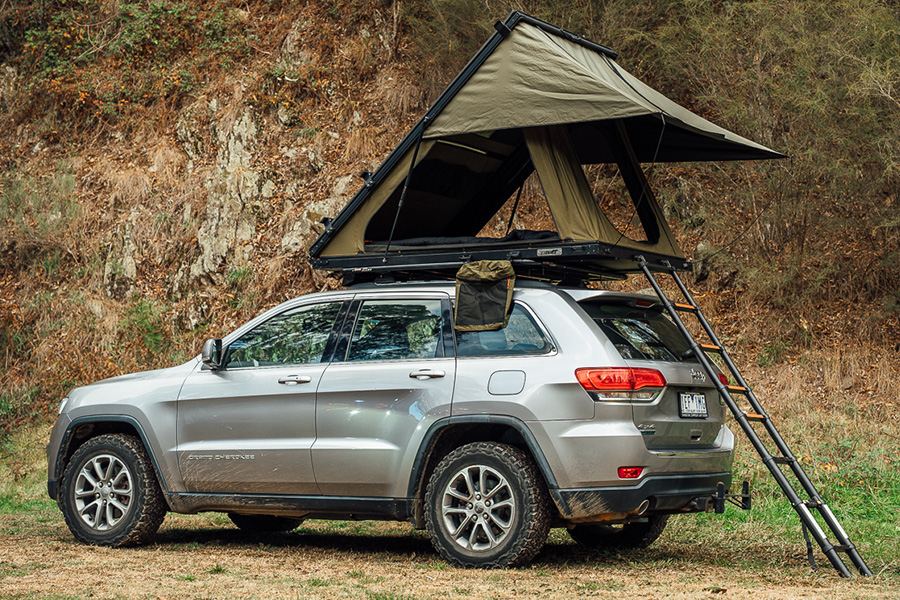 An SUV with a lightweight rooftop tent on top, and an extended ladder. 