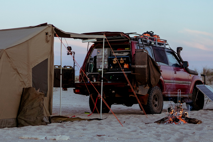 A 4WD and touring tent set up on a beach, with a campfire.