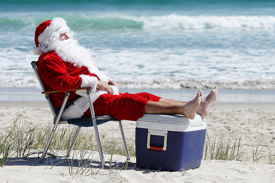 Santa on the beach kicking back with a cooler and a director's chair. 