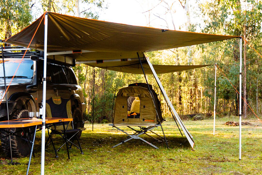 A campsite setup with a 4WD, swag, stretcher, camp table, and awning.