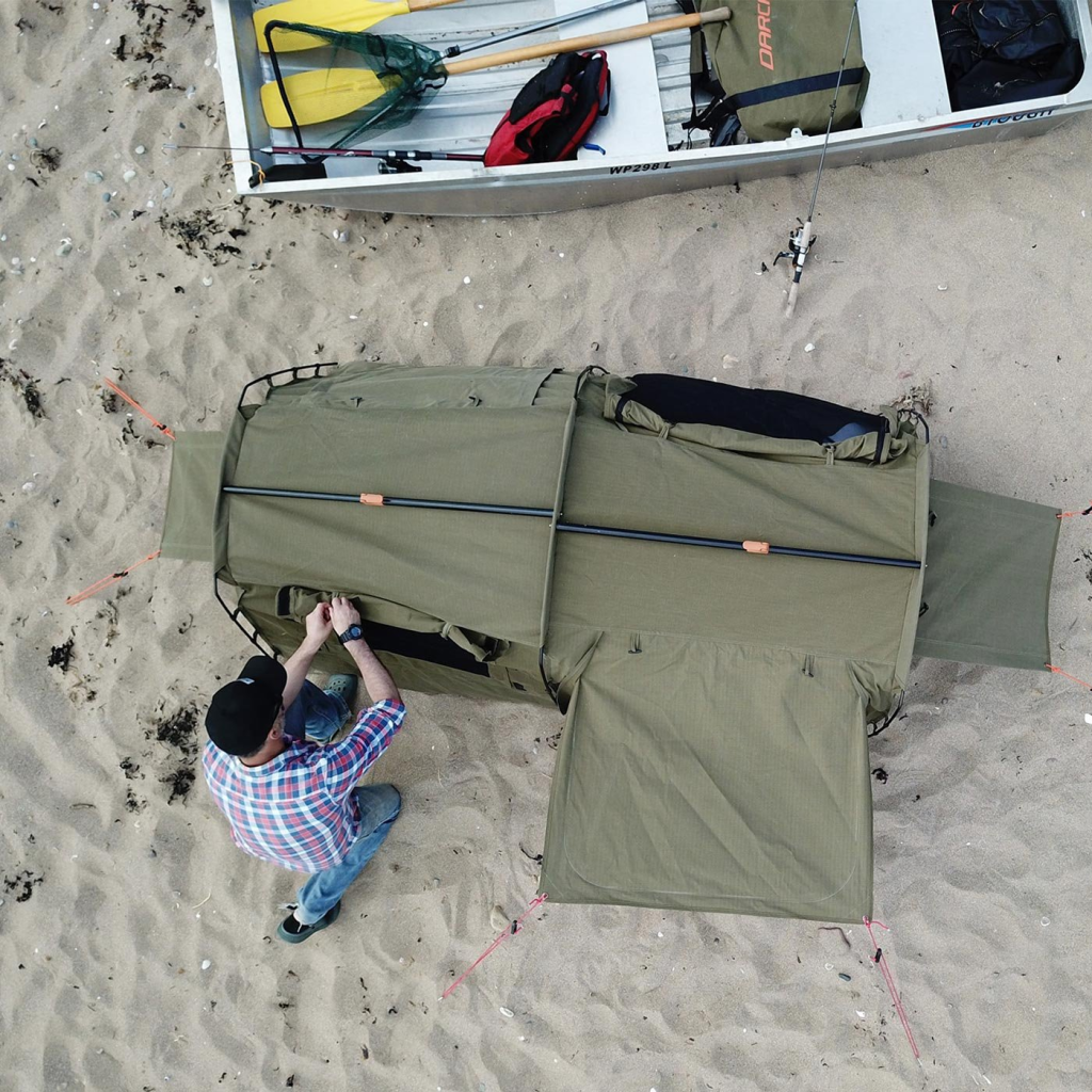 Aerial image of a man next to a swag on the beach with a tinnie boat nearby.